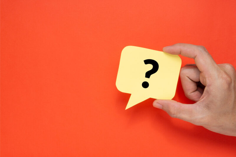 A man holding speech bubble with a question mark. Creative concept on red background.