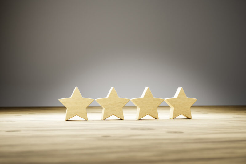 Four star rating: four wooden stars in a row on a wooden table with gray background. Selective focus. Concept shot for rating / reviews.