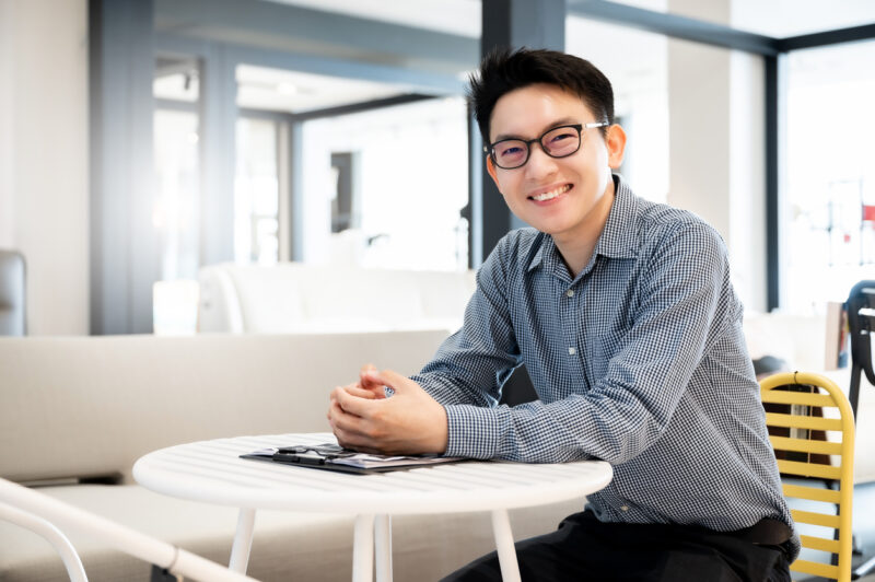 Happy young man sitting in modern office and looking at the camera with smile