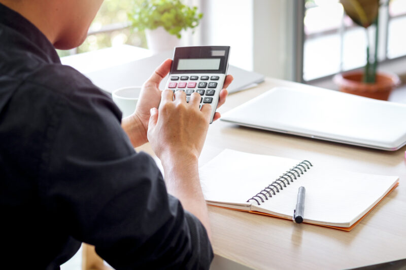 Businessman or accountant Asian young man holding calculator to calculate financial data, cost and budget on desk at home, accounting statistics and credit analytic for payment.