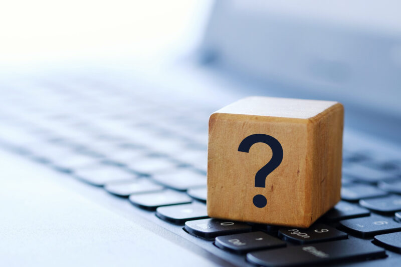 A question mark on a wooden cube on a computer keyboard, with a blurred background and shallow depth of field.