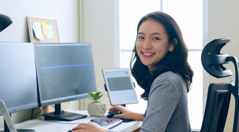 Portrait young Asian woman developer programmer, software engineer, IT support, look at camera and smile enjoy working at office.