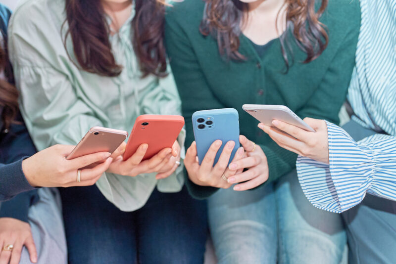 Four women talking while looking at their smartphones indoors